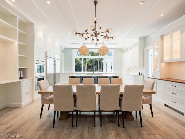 dining space with built in shelves, light wood-type flooring, and a notable chandelier