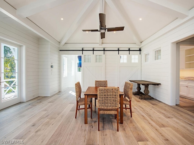 dining area with a barn door, wooden walls, beamed ceiling, and light hardwood / wood-style floors