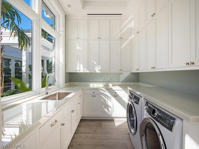 clothes washing area featuring cabinets, hardwood / wood-style floors, washer and clothes dryer, and sink