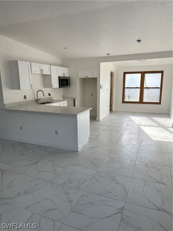 kitchen featuring vaulted ceiling, sink, kitchen peninsula, and white cabinetry