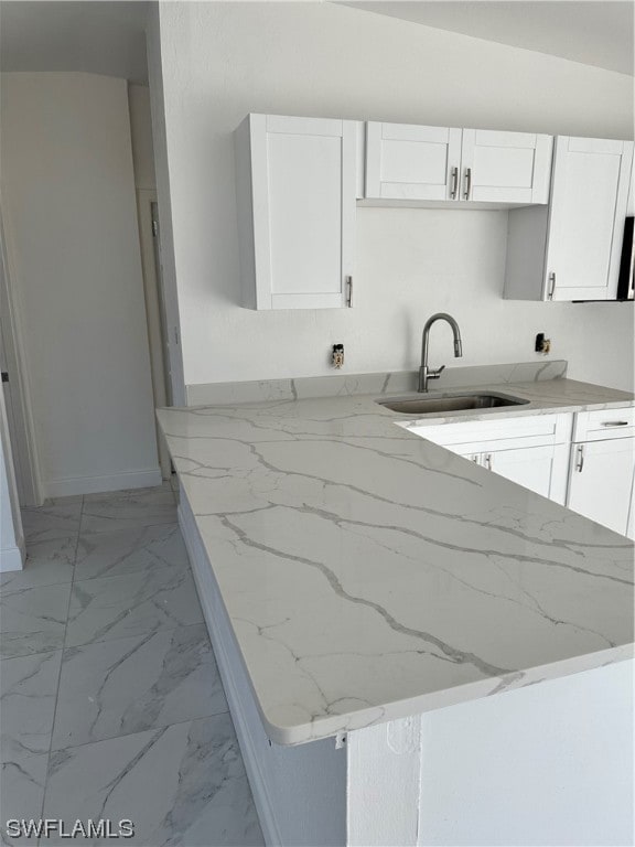 kitchen featuring light stone countertops, sink, kitchen peninsula, and white cabinetry