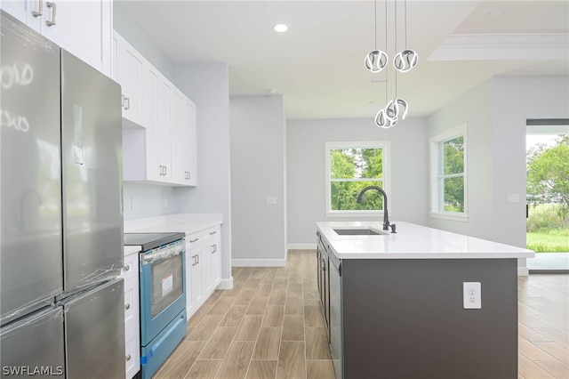 kitchen featuring stainless steel appliances, a kitchen island with sink, sink, decorative light fixtures, and white cabinetry