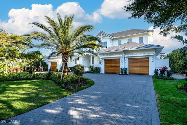 view of front of property featuring a garage, a tile roof, decorative driveway, and a front yard