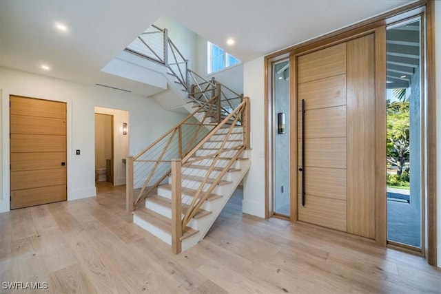 foyer with light wood finished floors, plenty of natural light, stairway, and baseboards