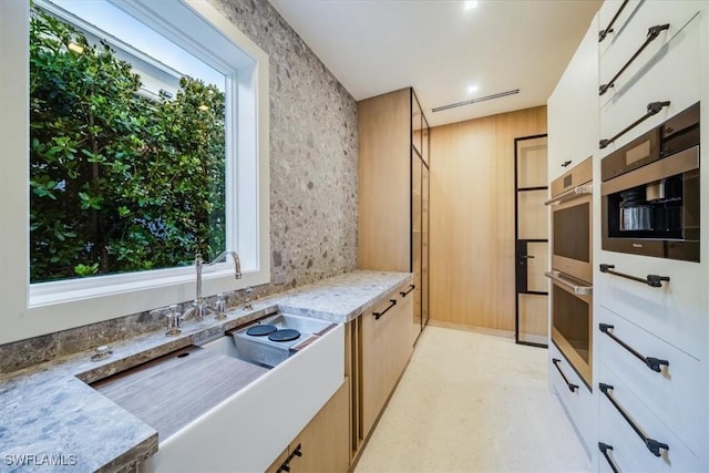 kitchen with white cabinets, light stone counters, a sink, light floors, and stainless steel double oven