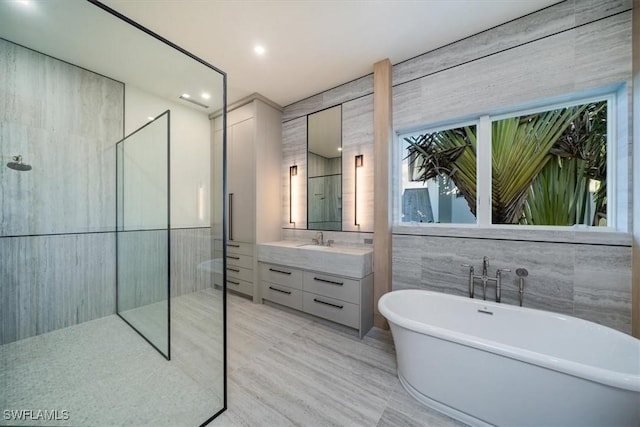 bathroom featuring a walk in shower, a freestanding tub, vanity, and tile walls