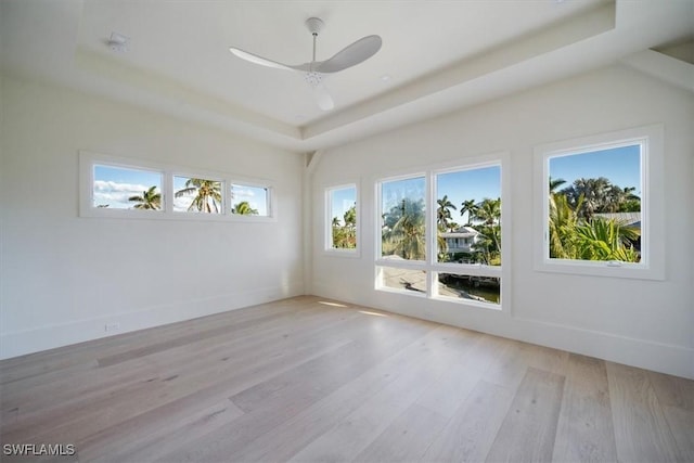 empty room featuring a raised ceiling, light wood-style floors, ceiling fan, and baseboards
