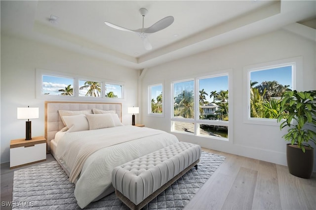 bedroom featuring baseboards, a raised ceiling, light wood-style floors, and a ceiling fan