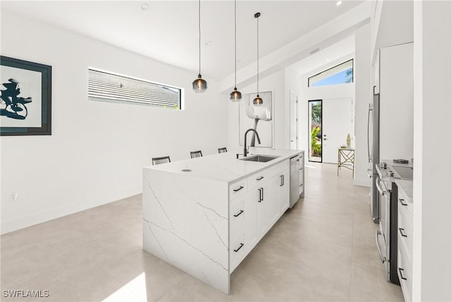 kitchen featuring light stone counters, stainless steel appliances, a sink, white cabinetry, and an island with sink