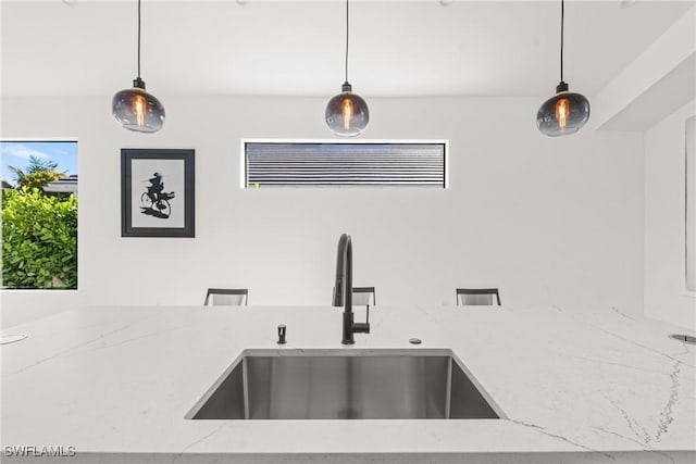 interior details featuring hanging light fixtures, light stone countertops, and a sink