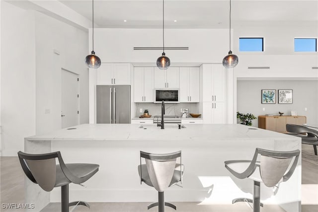 kitchen featuring a towering ceiling, white cabinetry, a sink, and freestanding refrigerator