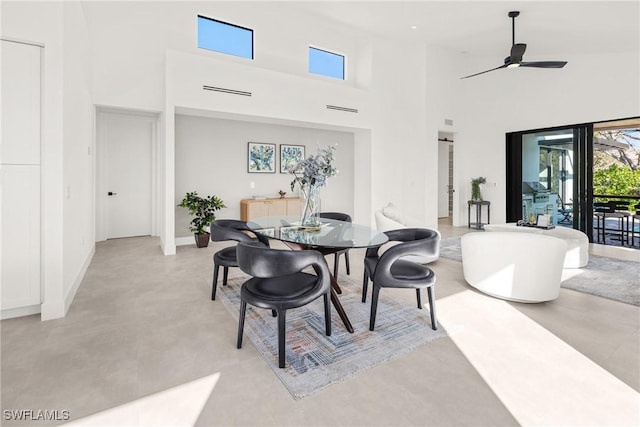 dining room with ceiling fan, a high ceiling, finished concrete floors, and baseboards