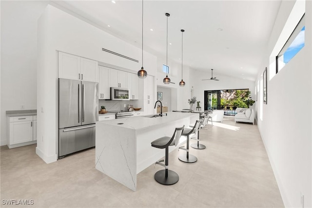 kitchen with stainless steel appliances, an island with sink, a towering ceiling, and white cabinetry
