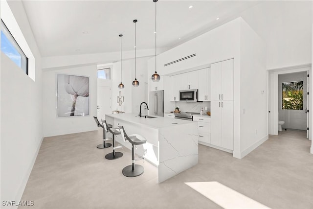 kitchen with concrete flooring, a breakfast bar area, stainless steel appliances, a sink, and white cabinets