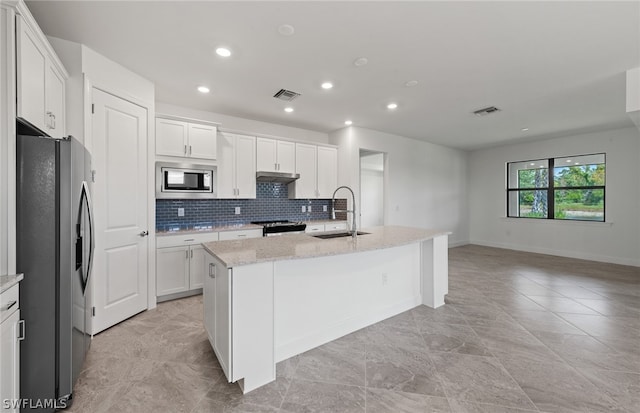 kitchen with stainless steel appliances, light stone countertops, an island with sink, sink, and light tile floors