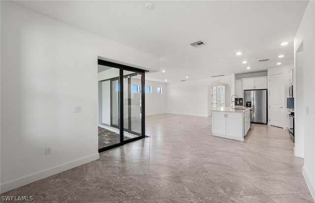 interior space featuring stainless steel refrigerator with ice dispenser, a kitchen island with sink, white cabinets, sink, and light tile floors