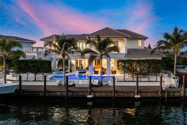 back house at dusk featuring outdoor lounge area, a patio, a water view, and a balcony