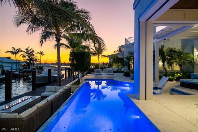 pool at dusk with outdoor lounge area, a water view, and a patio