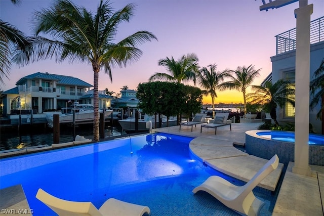 pool at dusk featuring an in ground hot tub and a patio