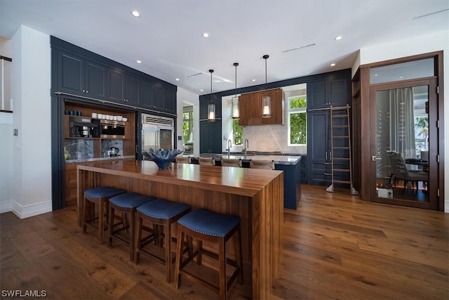 kitchen with built in refrigerator, decorative backsplash, decorative light fixtures, a kitchen island, and dark hardwood / wood-style flooring