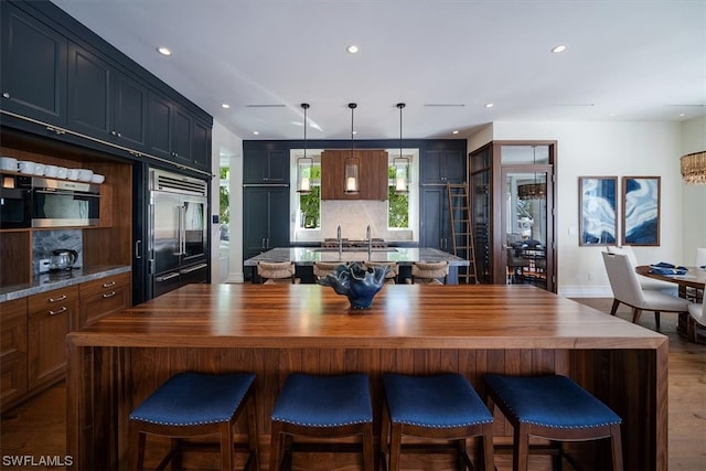 kitchen with a kitchen island, tasteful backsplash, hanging light fixtures, and built in refrigerator