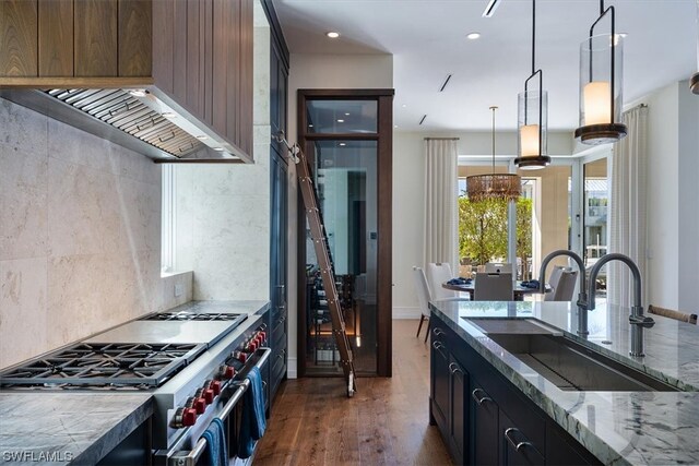 kitchen featuring wall chimney range hood, sink, stainless steel stove, light stone countertops, and dark hardwood / wood-style flooring