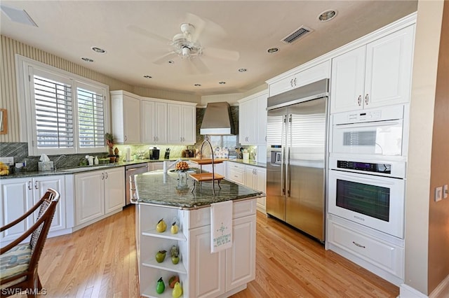kitchen with visible vents, dark stone countertops, white cabinetry, appliances with stainless steel finishes, and wall chimney range hood