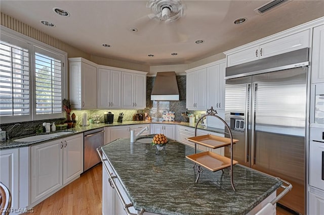 kitchen with a sink, appliances with stainless steel finishes, white cabinetry, wall chimney range hood, and a center island