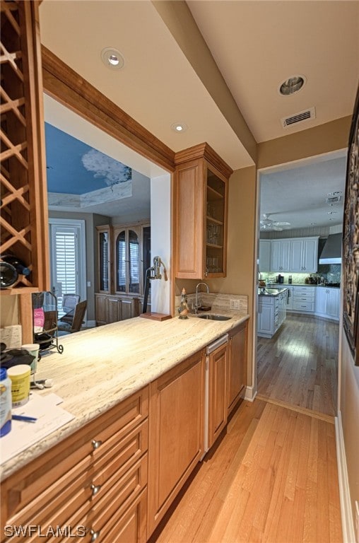 kitchen with light wood-type flooring, wall chimney range hood, sink, and light stone countertops