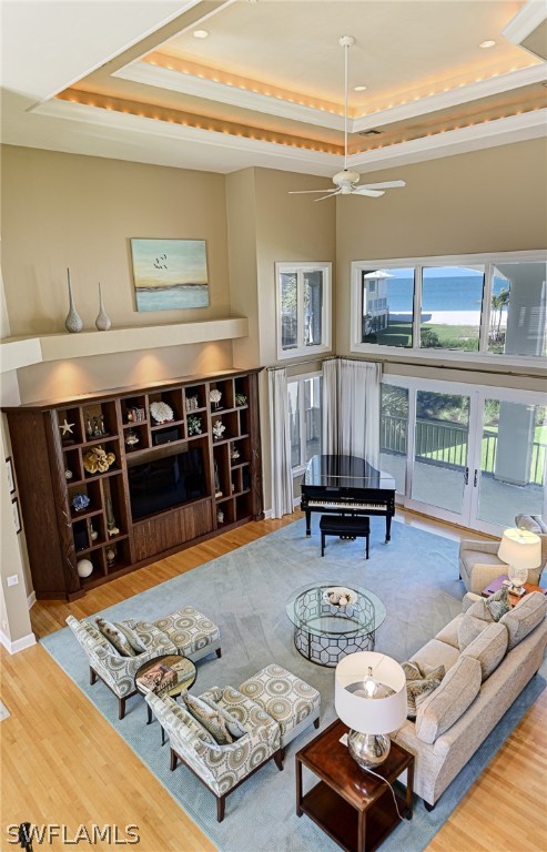 living room with light hardwood / wood-style flooring, ceiling fan, and a raised ceiling