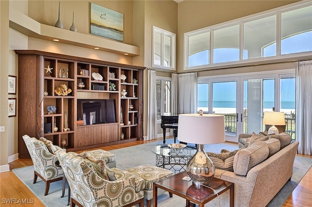 living area featuring french doors, a high ceiling, baseboards, and wood finished floors