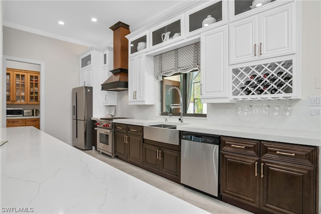 kitchen with crown molding, light stone countertops, custom range hood, appliances with stainless steel finishes, and white cabinetry