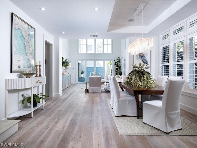 dining room with a tray ceiling, light hardwood / wood-style flooring, and an inviting chandelier