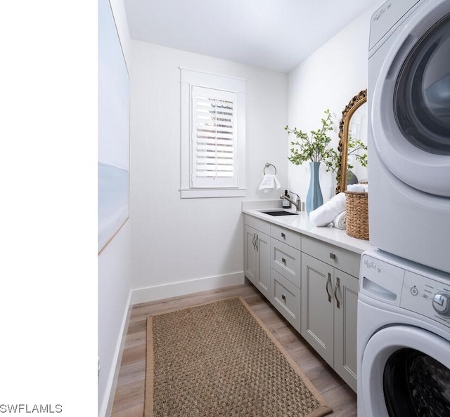 laundry room with cabinets, stacked washer and dryer, sink, and light hardwood / wood-style flooring