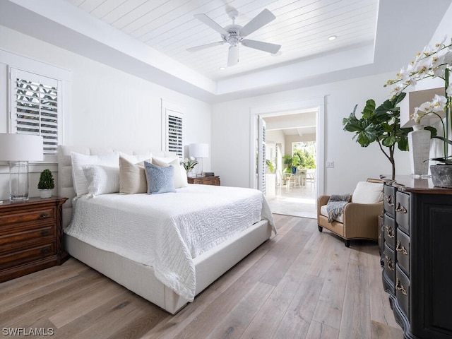 bedroom with a raised ceiling, ceiling fan, and light hardwood / wood-style flooring