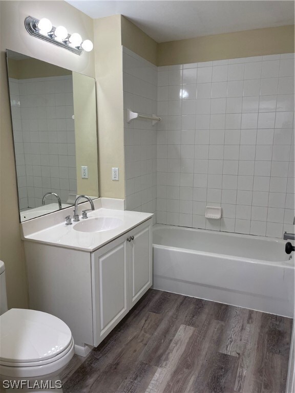 bathroom featuring toilet, shower / bathtub combination, wood finished floors, and vanity