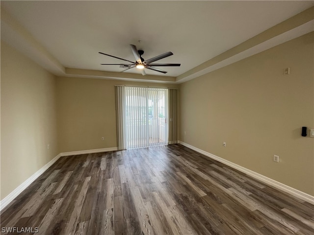 spare room with a ceiling fan, baseboards, a tray ceiling, and dark wood-type flooring