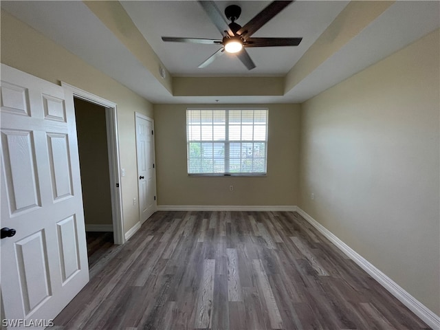 unfurnished bedroom featuring a ceiling fan, baseboards, a tray ceiling, and dark wood-style flooring