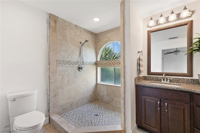 bathroom featuring toilet, ceiling fan, tiled shower, tile flooring, and vanity