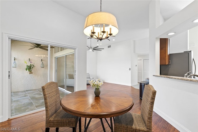 dining space featuring ceiling fan with notable chandelier, sink, and dark wood-type flooring