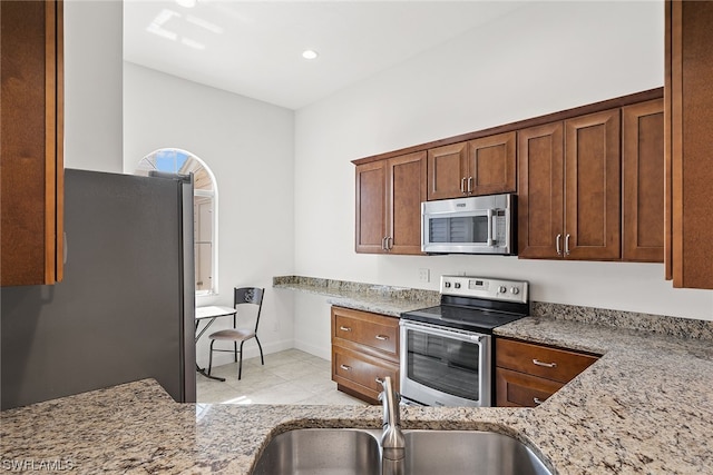 kitchen with light tile floors, light stone countertops, sink, and stainless steel appliances