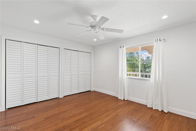 unfurnished bedroom with multiple closets, ceiling fan, and dark wood-type flooring