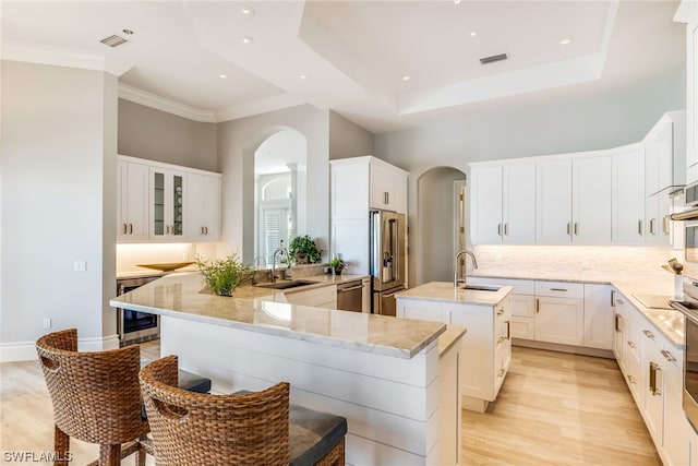 kitchen with kitchen peninsula, appliances with stainless steel finishes, sink, a center island with sink, and light hardwood / wood-style floors