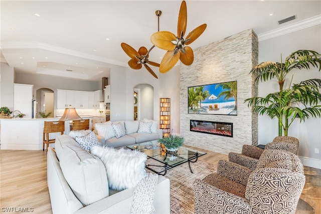 living room featuring a fireplace, light hardwood / wood-style floors, ceiling fan, and ornamental molding