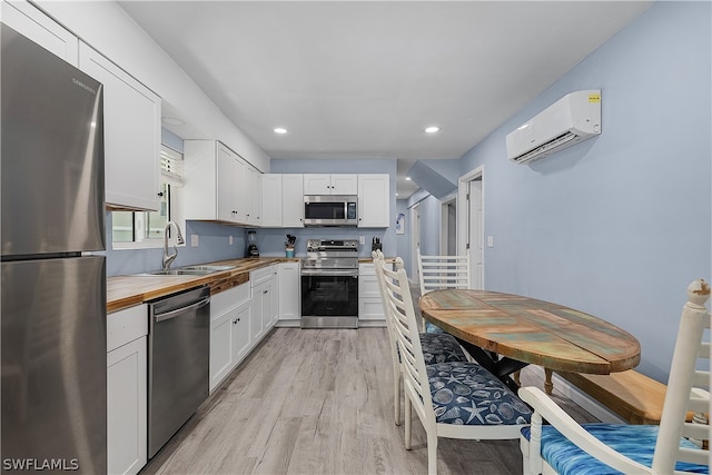 kitchen featuring white cabinets, a wall mounted air conditioner, stainless steel appliances, and light wood-type flooring