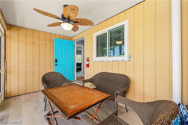 sitting room with wood walls, ceiling fan, and light wood-type flooring