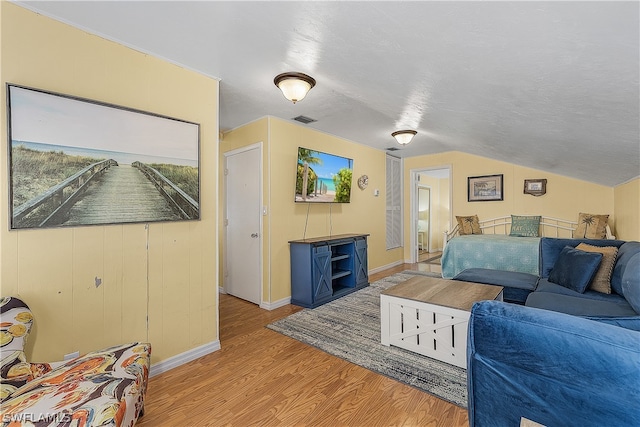 living room featuring a textured ceiling, light hardwood / wood-style floors, and vaulted ceiling