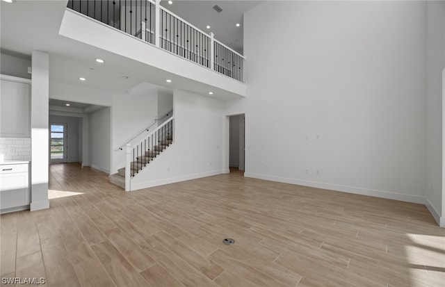 unfurnished living room featuring light hardwood / wood-style flooring and a towering ceiling