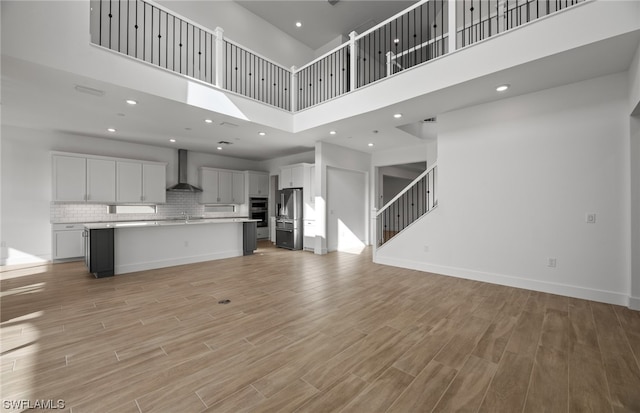 unfurnished living room with a towering ceiling, sink, and light wood-type flooring