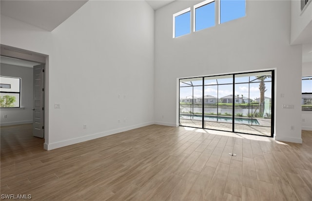 spare room featuring plenty of natural light, light hardwood / wood-style floors, a towering ceiling, and a water view